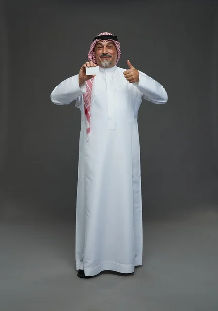رجل  عربي سعودي خليجي مسن يرتدي الزي الثوب الابيض والشماغ ويمسك بطاقه بيضاء فارغه,  ايماءات واشارات مختلفه , كامل الجسم, خلفيه رماديه
