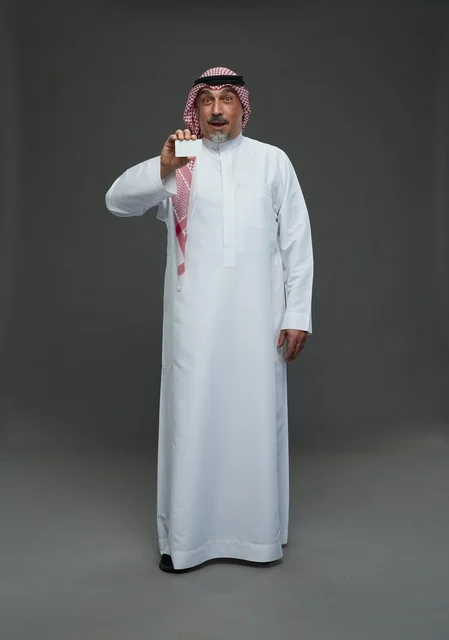 رجل  عربي سعودي خليجي مسن يرتدي الزي الثوب الابيض والشماغ ويمسك بطاقه بيضاء فارغه,  ايماءات واشارات مختلفه , كامل الجسم, خلفيه رماديه