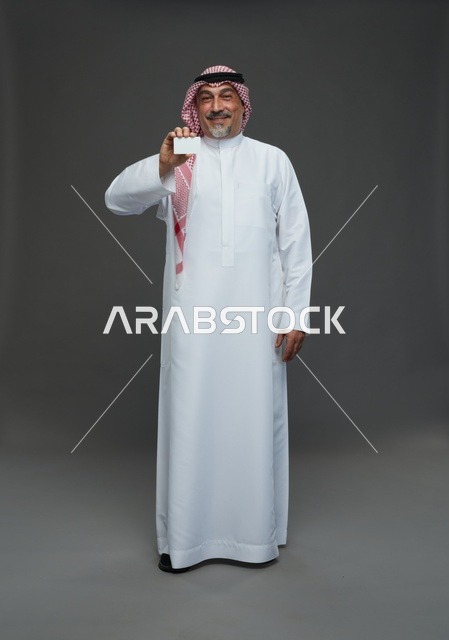 رجل  عربي سعودي خليجي مسن يرتدي الزي الثوب الابيض والشماغ ويمسك بطاقه بيضاء فارغه,  ايماءات واشارات مختلفه , كامل الجسم, خلفيه رماديه