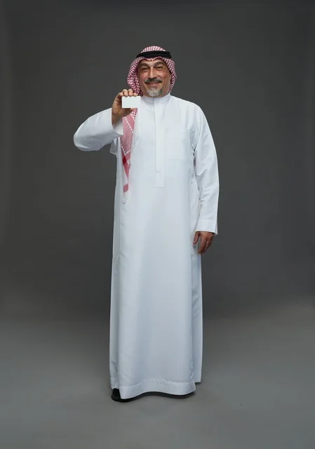 رجل  عربي سعودي خليجي مسن يرتدي الزي الثوب الابيض والشماغ ويمسك بطاقه بيضاء فارغه,  ايماءات واشارات مختلفه , كامل الجسم, خلفيه رماديه