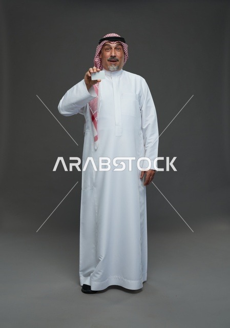 رجل  عربي سعودي خليجي مسن يرتدي الزي الثوب الابيض والشماغ ويمسك بطاقه بيضاء فارغه,  ايماءات واشارات مختلفه , كامل الجسم, خلفيه رماديه