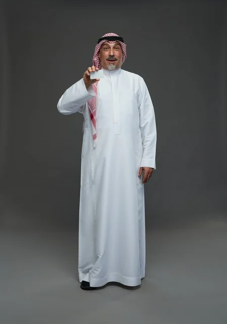 An elderly Arab Saudi Gulf man wearing a white thobe and a shemagh, holding a blank white card, with various gestures and signs, full body, gray background.