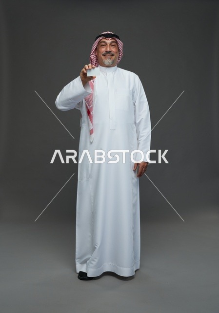 رجل  عربي سعودي خليجي مسن يرتدي الزي الثوب الابيض والشماغ ويمسك بطاقه بيضاء فارغه,  ايماءات واشارات مختلفه , كامل الجسم, خلفيه رماديه