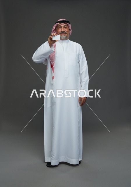 رجل  عربي سعودي خليجي مسن يرتدي الزي الثوب الابيض والشماغ ويمسك بطاقه بيضاء فارغه,  ايماءات واشارات مختلفه , كامل الجسم, خلفيه رماديه