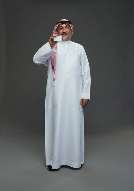 An elderly Arab Saudi Gulf man wearing a white thobe and a shemagh, holding a blank white card, with various gestures and signs, full body, gray background.
