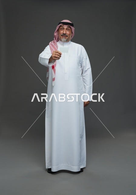رجل  عربي سعودي خليجي مسن يرتدي الزي الثوب الابيض والشماغ ويمسك بطاقه بيضاء فارغه,  ايماءات واشارات مختلفه , كامل الجسم, خلفيه رماديه