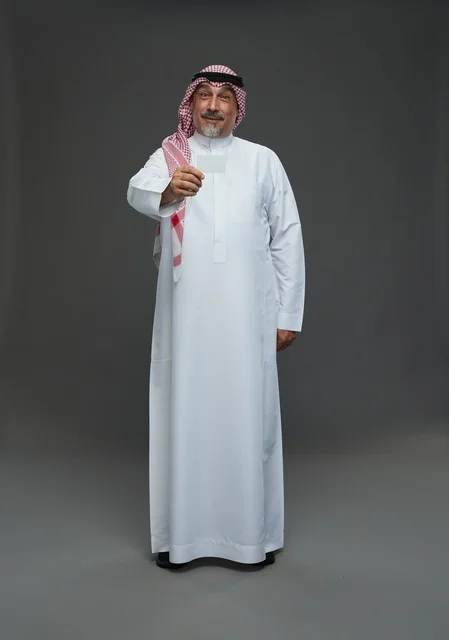 An elderly Arab Saudi Gulf man wearing a white thobe and a shemagh, holding a blank white card, with various gestures and signs, full body, gray background.
