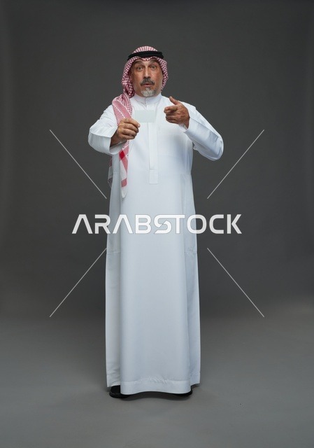 رجل  عربي سعودي خليجي مسن يرتدي الزي الثوب الابيض والشماغ ويمسك بطاقه بيضاء فارغه,  ايماءات واشارات مختلفه , كامل الجسم, خلفيه رماديه