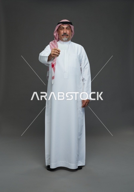 رجل  عربي سعودي خليجي مسن يرتدي الزي الثوب الابيض والشماغ ويمسك بطاقه بيضاء فارغه,  ايماءات واشارات مختلفه , كامل الجسم, خلفيه رماديه