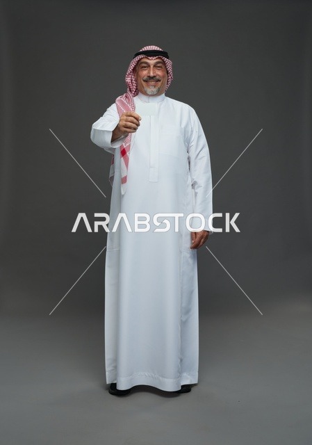 رجل  عربي سعودي خليجي مسن يرتدي الزي الثوب الابيض والشماغ ويمسك بطاقه بيضاء فارغه,  ايماءات واشارات مختلفه , كامل الجسم, خلفيه رماديه