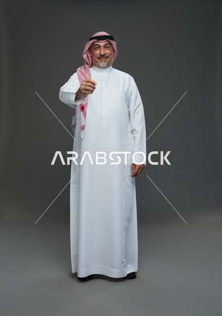 رجل  عربي سعودي خليجي مسن يرتدي الزي الثوب الابيض والشماغ ويمسك بطاقه بيضاء فارغه,  ايماءات واشارات مختلفه , كامل الجسم, خلفيه رماديه
