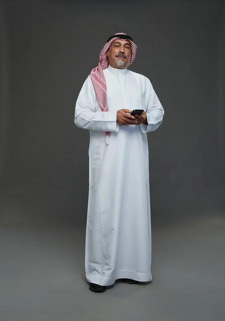 An elderly Arab Saudi Gulf man wearing a white thobe and a shemagh, holding a mobile phone, with various gestures and signals, full body, gray background.