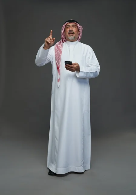 رجل  عربي سعودي خليجي مسن يرتدي الزي الثوب الابيض والشماغ ويمسك الهاتف المحمول,  ايماءات واشارات مختلفه , كامل الجسم, خلفيه رماديه