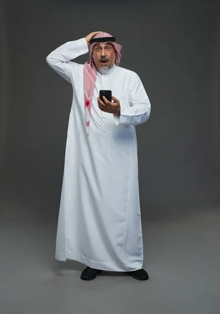 An elderly Arab Saudi Gulf man wearing a white thobe and a shemagh, holding a mobile phone, with various gestures and signals, full body, gray background.