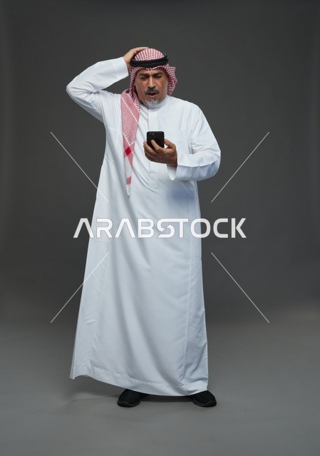 رجل  عربي سعودي خليجي مسن يرتدي الزي الثوب الابيض والشماغ ويمسك الهاتف المحمول,  ايماءات واشارات مختلفه , كامل الجسم, خلفيه رماديه