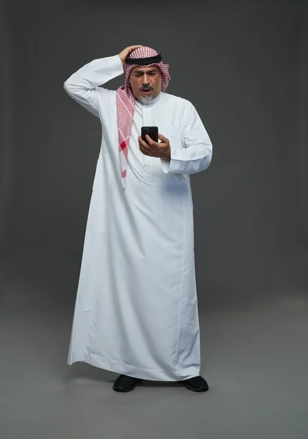 رجل  عربي سعودي خليجي مسن يرتدي الزي الثوب الابيض والشماغ ويمسك الهاتف المحمول,  ايماءات واشارات مختلفه , كامل الجسم, خلفيه رماديه