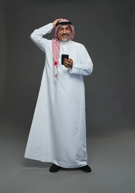 An elderly Arab Saudi Gulf man wearing a white thobe and a shemagh, holding a mobile phone, with various gestures and signals, full body, gray background.