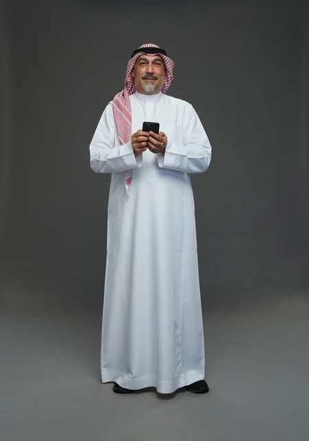 رجل  عربي سعودي خليجي مسن يرتدي الزي الثوب الابيض والشماغ ويمسك الهاتف المحمول,  ايماءات واشارات مختلفه , كامل الجسم, خلفيه رماديه