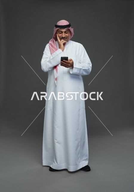 رجل  عربي سعودي خليجي مسن يرتدي الزي الثوب الابيض والشماغ ويمسك الهاتف المحمول,  ايماءات واشارات مختلفه , كامل الجسم, خلفيه رماديه