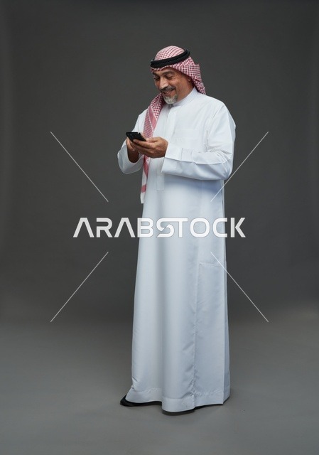 رجل  عربي سعودي خليجي مسن يرتدي الزي الثوب الابيض والشماغ ويمسك الهاتف المحمول,  ايماءات واشارات مختلفه , كامل الجسم, خلفيه رماديه