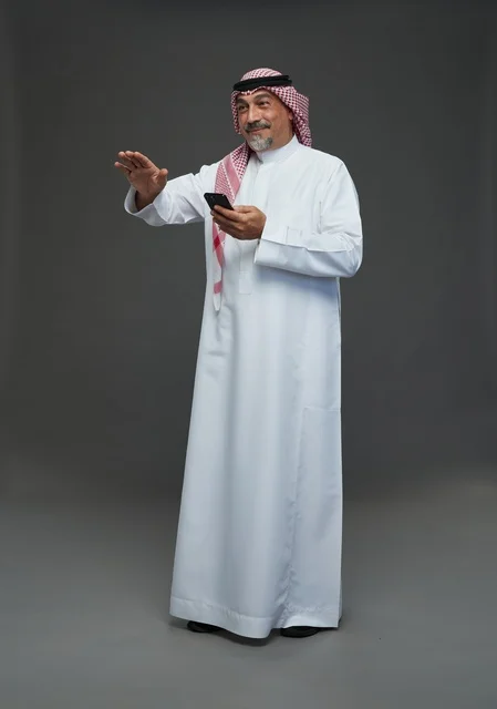 An elderly Arab Saudi Gulf man wearing a white thobe and a shemagh, holding a mobile phone, with various gestures and signals, full body, gray background.
