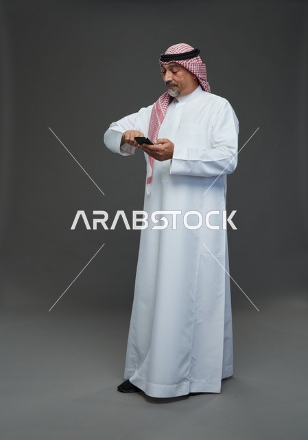 An elderly Arab Saudi Gulf man wearing a white thobe and a shemagh, holding a mobile phone, with various gestures and signals, full body, gray background.