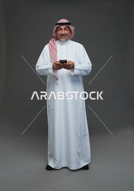 رجل  عربي سعودي خليجي مسن يرتدي الزي الثوب الابيض والشماغ ويمسك الهاتف المحمول,  ايماءات واشارات مختلفه , كامل الجسم, خلفيه رماديه