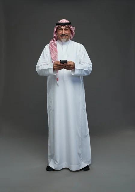 رجل  عربي سعودي خليجي مسن يرتدي الزي الثوب الابيض والشماغ ويمسك الهاتف المحمول,  ايماءات واشارات مختلفه , كامل الجسم, خلفيه رماديه