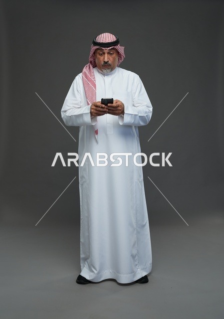 An elderly Arab Saudi Gulf man wearing a white thobe and a shemagh, holding a mobile phone, with various gestures and signals, full body, gray background.