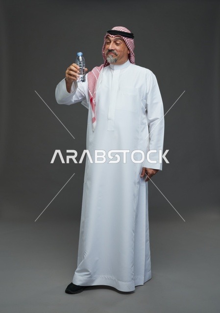 رجل  عربي سعودي خليجي مسن يرتدي الزي الثوب الابيض والشماغ ويحمل قارورة ماء,  ايماءات واشارات مختلفه , كامل الجسم, خلفيه رماديه
