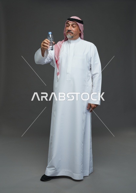 رجل  عربي سعودي خليجي مسن يرتدي الزي الثوب الابيض والشماغ ويحمل قارورة ماء,  ايماءات واشارات مختلفه , كامل الجسم, خلفيه رماديه