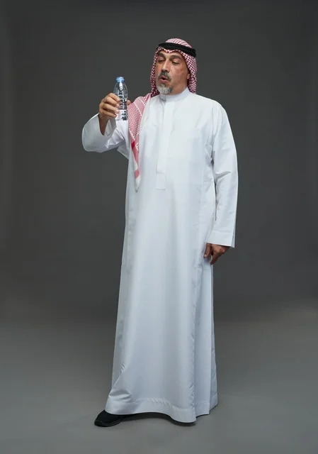 An elderly Arab Saudi Gulf man wearing a white thobe and a shemagh, holding a water bottle, with various gestures and signs, full body, gray background.