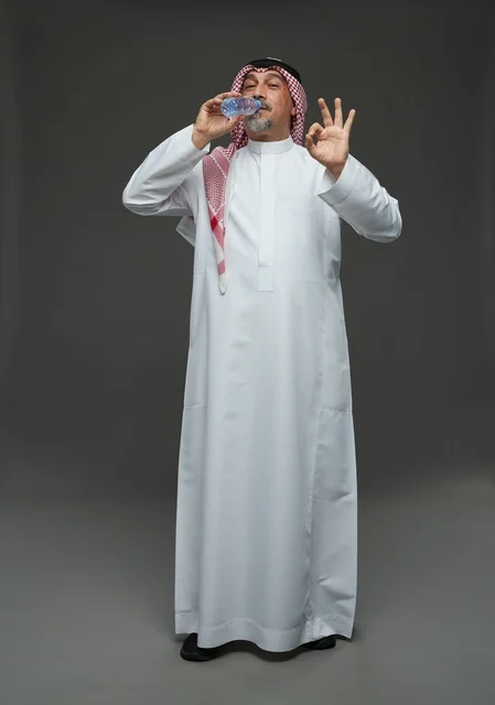 An elderly Arab Saudi Gulf man wearing a white thobe and a shemagh, holding a water bottle, with various gestures and signs, full body, gray background.