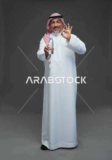 رجل  عربي سعودي خليجي مسن يرتدي الزي الثوب الابيض والشماغ ويحمل قارورة ماء,  ايماءات واشارات مختلفه , كامل الجسم, خلفيه رماديه