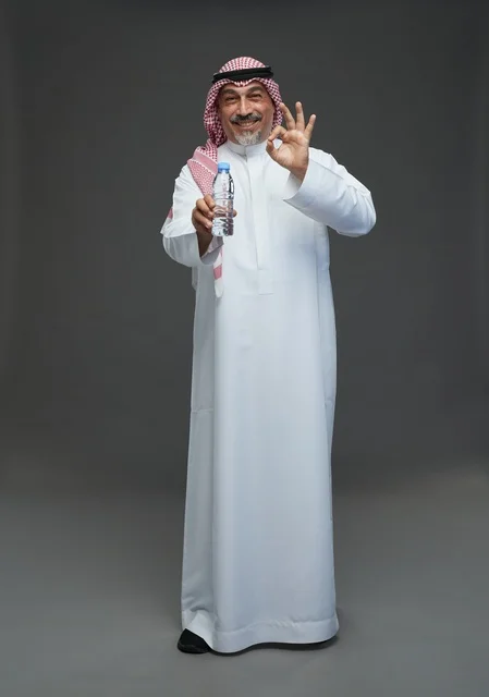An elderly Arab Saudi Gulf man wearing a white thobe and a shemagh, holding a water bottle, with various gestures and signs, full body, gray background.