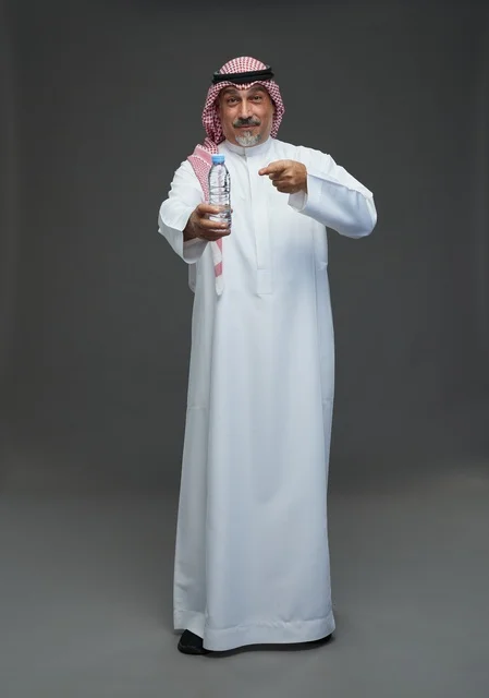 رجل  عربي سعودي خليجي مسن يرتدي الزي الثوب الابيض والشماغ ويحمل قارورة ماء,  ايماءات واشارات مختلفه , كامل الجسم, خلفيه رماديه