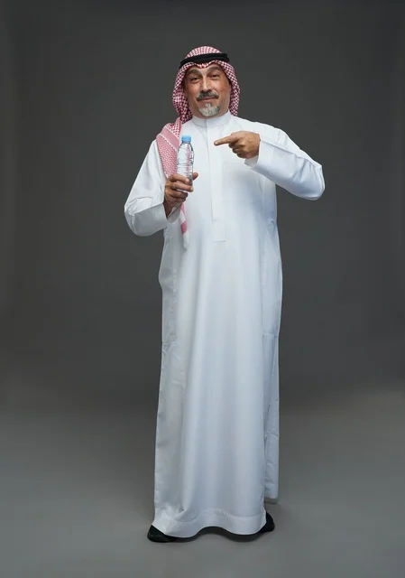 An elderly Arab Saudi Gulf man wearing a white thobe and a shemagh, holding a water bottle, with various gestures and signs, full body, gray background.