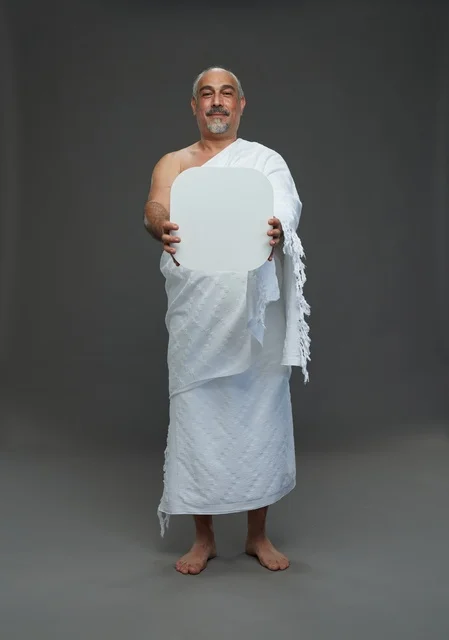 بورتريه لحاج سعودي بملابس الإحرام يحمل لوح مربع ابيض فارغ أثناء أداء المناسك, ايماءات واشارات مختلفه, كامل الجسم, خلفيه رماديه