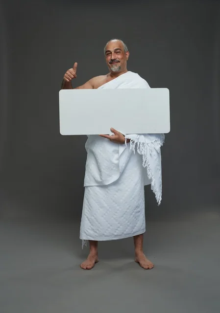 بورتريه لحاج سعودي بملابس الإحرام يحمل لوح مربع ابيض فارغ أثناء أداء المناسك, ايماءات واشارات مختلفه, كامل الجسم, خلفيه رماديه