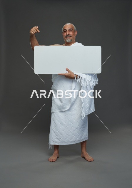 بورتريه لحاج سعودي بملابس الإحرام يحمل لوح مربع ابيض فارغ أثناء أداء المناسك, ايماءات واشارات مختلفه, كامل الجسم, خلفيه رماديه