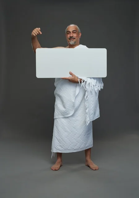 A portrait of a Saudi pilgrim in Ihram clothing holding a blank white square board while performing the rituals, with various gestures and signs, full body, gray background.