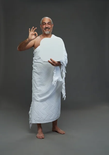 بورتريه لحاج سعودي بملابس الإحرام يحمل لوح مربع ابيض فارغ أثناء أداء المناسك, ايماءات واشارات مختلفه, كامل الجسم, خلفيه رماديه
