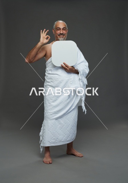 A portrait of a Saudi pilgrim in Ihram clothing holding a blank white square board while performing the rituals, with various gestures and signs, full body, gray background.