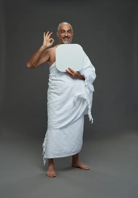 بورتريه لحاج سعودي بملابس الإحرام يحمل لوح مربع ابيض فارغ أثناء أداء المناسك, ايماءات واشارات مختلفه, كامل الجسم, خلفيه رماديه