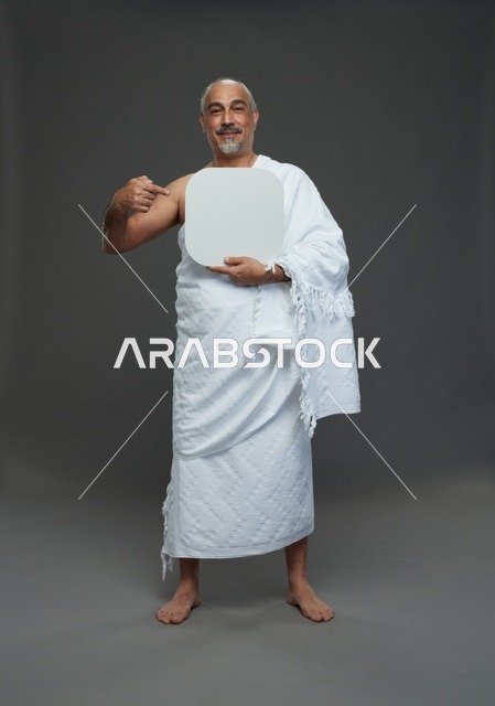 A portrait of a Saudi pilgrim in Ihram clothing holding a blank white square board while performing the rituals, with various gestures and signs, full body, gray background.