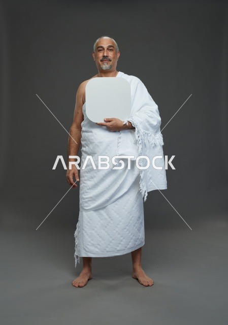 A portrait of a Saudi pilgrim in Ihram clothing holding a blank white square board while performing the rituals, with various gestures and signs, full body, gray background.