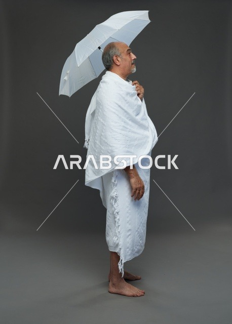 A portrait of a Saudi man in Ihram clothing holding a white umbrella while performing rituals, with various gestures and signals, full body, gray background.