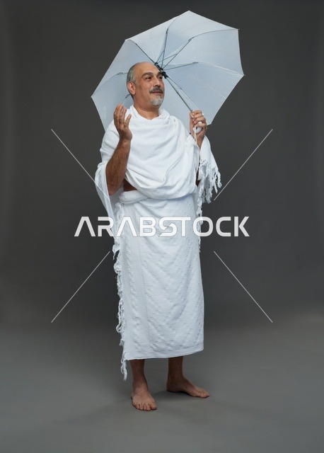 A portrait of a Saudi man in Ihram clothing holding a white umbrella while performing rituals, with various gestures and signals, full body, gray background.