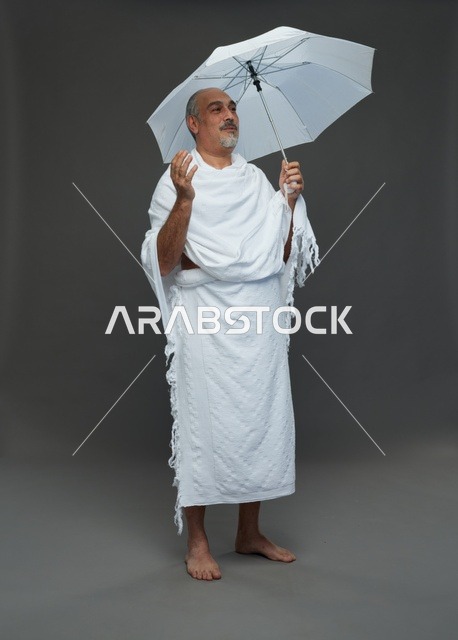 A portrait of a Saudi man in Ihram clothing holding a white umbrella while performing rituals, with various gestures and signals, full body, gray background.