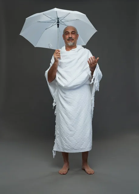 A portrait of a Saudi man in Ihram clothing holding a white umbrella while performing rituals, with various gestures and signals, full body, gray background.